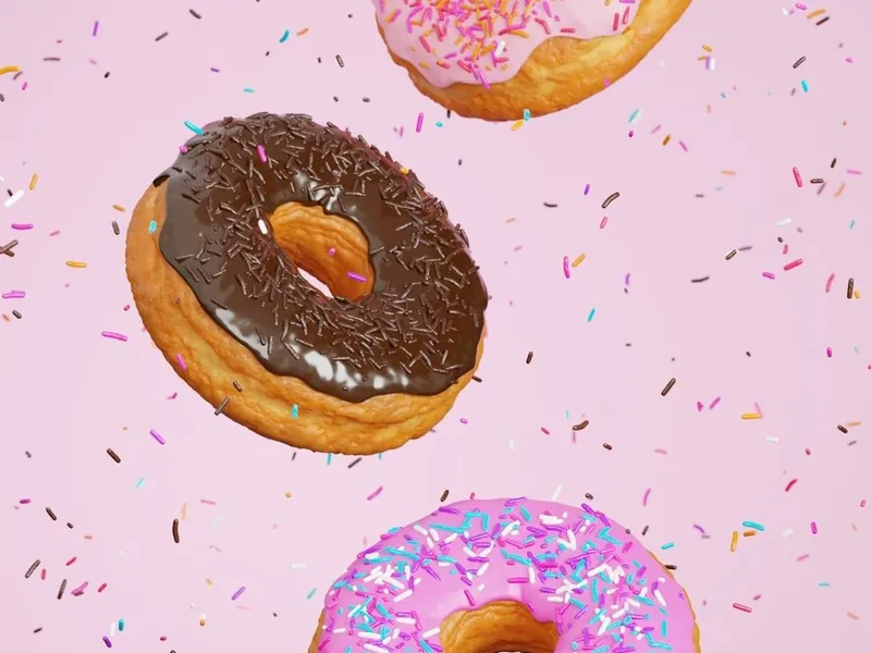 Three frosted donuts with sprinkles floating against a pink background.